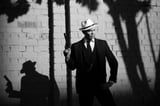 Stylish man in vintage suit and fedora hat holding a revolver, classic film noir aesthetic